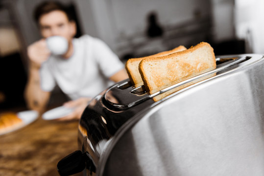 young man drinking coffee at home with toaster on foreground