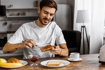 Fototapeta na wymiar happy young man applying jam onto toast at home