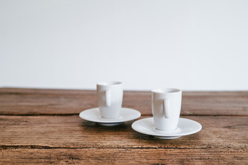 2 Espresso Tassen Henkel vorne auf Unterteller Holztisch Hintergrund weiß