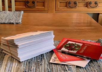 Stack of Christmas greeting cards ready to be placed in the mail with a few cards and pen laying next to them on country kitchen table