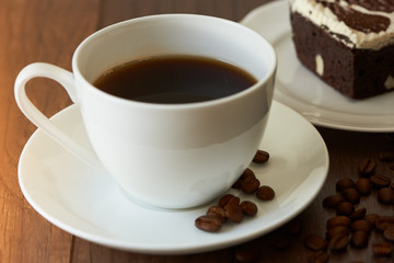 A tasty cup of hot coffee and a piece of chocolate cake on wooden table