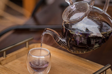 Purple floral herbal tea is poured from the brewer into the cup.