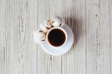 A cup of coffee with cotton on a wooden background.