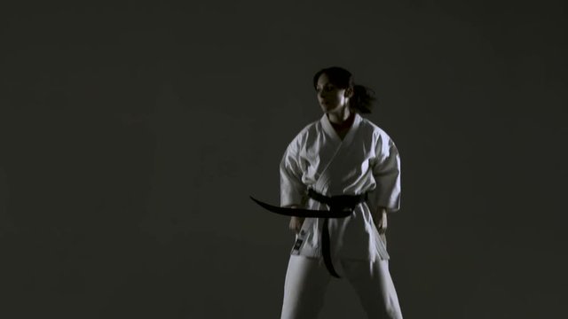 karate girl practicing multiple jump kicks, wearing kimono, on dark background. slow motion recorded at 120fps

