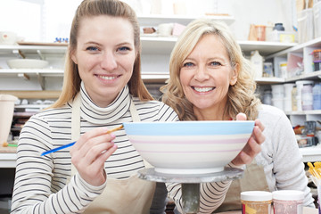 Portrait Of Woman Decorating Bowl With Teacher In Pottery Class