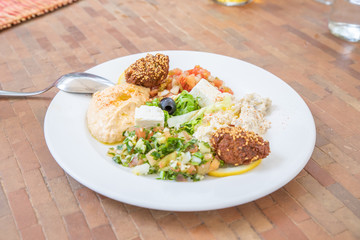 mezze or meze, selection of typical Arabic appetizers (hummus, falafel, baba ghanoush, Feta cheese, Marrakesh salad, tabule, olives) on a white dish with spoon on table