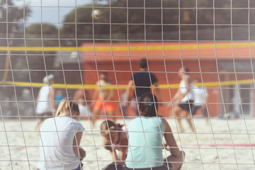 Group of young friends playing beach volleyball, unrecognizable girl fans back to us, summer day, selectiv focus