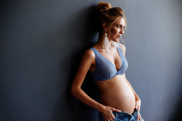 Beautiful pregnant young woman near the wall.