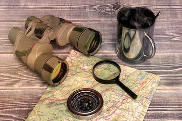 binoculars, map, magnifying glass, compass, tea mug on wooden background. tourism, recreation.