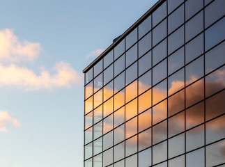 sky is reflected in the modern glass facade of the building