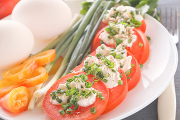 Sliced tomatoes with cheese and herbs on a white plate with onions, sweet peppers and eggs. Close-up