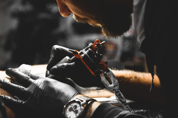 The tattoo artist creates a picture on the body of a man. close-up of tattoo machines and hands - obrazy, fototapety, plakaty