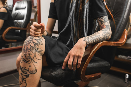 girl with dreadlocks in a tattoo parlor. The master creates a picture on the body of a young beautiful girl. Close-up of hands and tattoo machine
