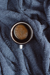 Winter or autumn cozy concept. Cup of coffee  on  blue knitted sweater. Flat lay, top view.