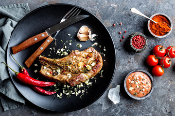 fried pork steak with garlic and thyme in dark plate on dark background