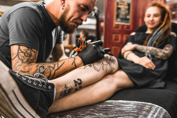 girl with dreadlocks in a tattoo parlor. The master creates a picture on the body of a young beautiful girl. Close-up of hands and tattoo machine