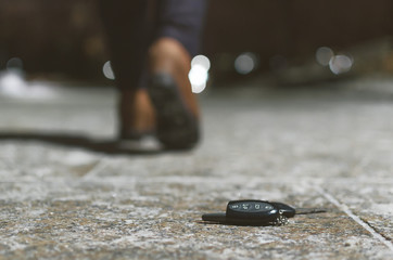 Car keys dropped from a woman pocket on the night footpath and her silhouette is walking away.