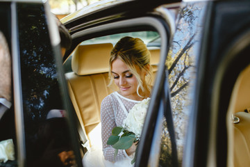 A bride takes pictures in the black car.