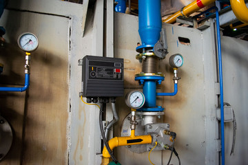 Gauges in the boiler room near the heating pipes with insulation coating. Electric power meter...