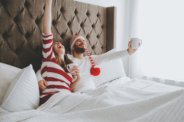 Loving couple snuggling in bed with Christmas attire and mugs