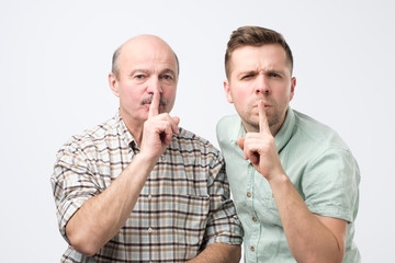 Two mature men keep fore finger on lips, tries to keep conspiracy