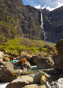 Resting tourist sitting on the big stone with a high waterfall on bacground, valley of Gavarnie, Pyrenees Occidentales, France
