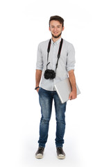 Fototapeta premium Nerd boy with camera around his neck and computer under his arm, he is standing in the studio and is wearing casual clothes