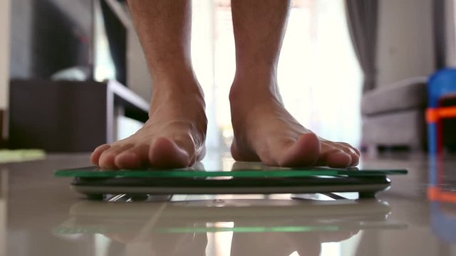 Close up men barefoot legs stepping on flooring scales for weighting in living room.