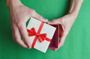 Present gift box with red ribbon in male hands on green background.