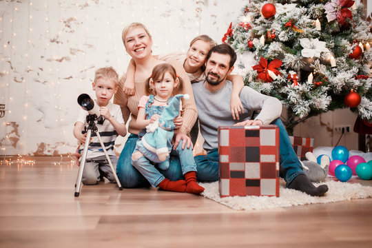 Image of happy family sitting with gift box at decorated Christmas tree