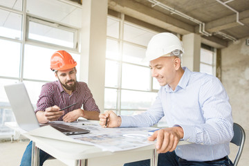 male engineers, architects working at the desk in helmets. Drawings, laptop, roulette on the...