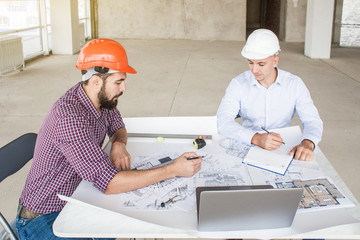 male engineers, architects working at the desk in helmets. Drawings, laptop, roulette on the desktop. Reception and supervision of building construction