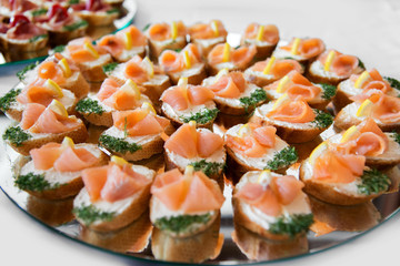 Close up of small canapes arranged on a plate over light background - selective focus