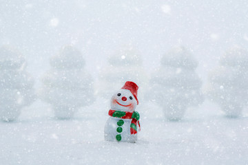 Miniature people in Christmas Theme. Happy snowman on snow with background of blurred christmas pine 