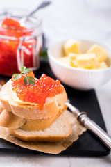 Salmon red caviarin a glass jar and Sandwiches with butter and parsley on slate cutting board on a light marble background. Seafood. Healthy Food Concept. Snack.