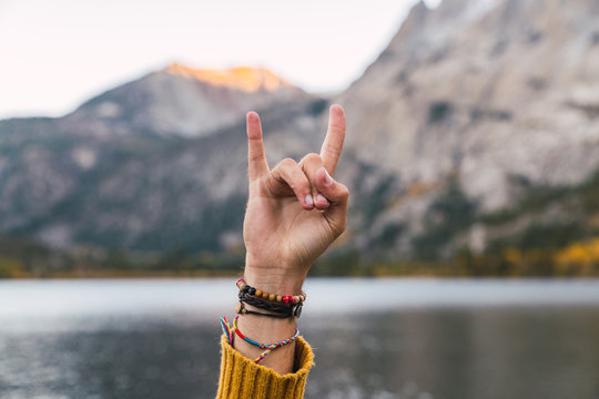 Person showing devil horns gesture near lake