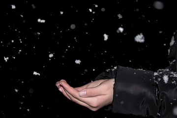 Women's hands catch falling snowflakes, dark time