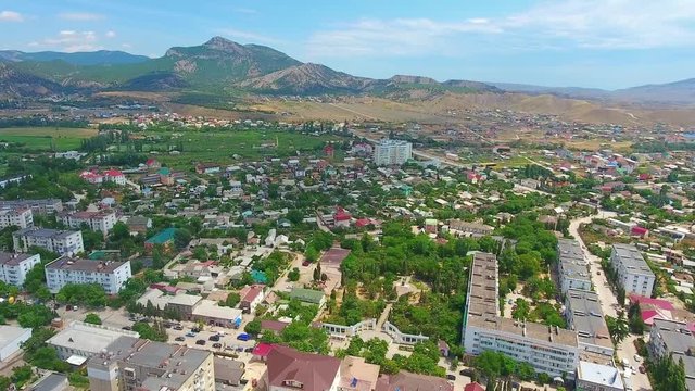 Aerial view of beautiful cityskype, centre, street, green mountains, Crimea. Drone footage of city-resort Sudak coastline with sea and hotels, buildings and beach.