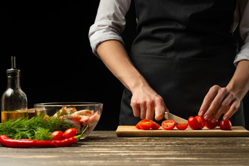 Professional chef slices cherry tomatoes for shrimp with vegetables,the concept of seafood and healthy food. Horizontal photo, menu, recipe book