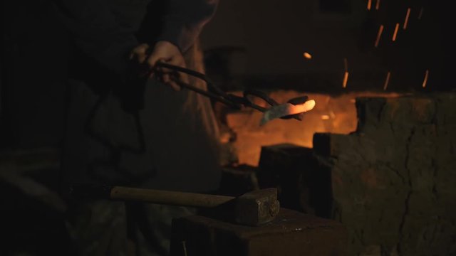 blacksmith works metal. Craftsman, the Highlander on private smithy in the village. Hot rod puts on the anvil, the master hits him with a sledgehammer. On the blacksmith's forge lies a sledgehammer