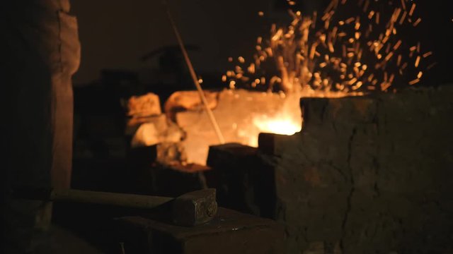 blacksmith works metal. Craftsman, the Highlander on private smithy in the village. Craftsman interferes with embers in the furnace. Hands are dressed in fire resistant mittens. Sparks fly apart. 2000