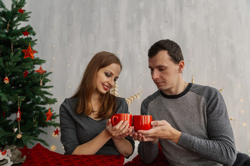 Family couple on the bed in the New Year's room holding red mugs with tea.