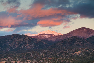 Dramatic, beautiful sunset casts purple and orange colors on clouds and the snow-capped peak of Santa Fe Baldy over a neighborhood in Tesuque, near Santa Fe, New Mexico