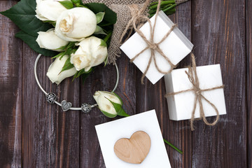 White gift boxes of a famous jewelry brand, a small bouquet of white roses and a silver bracelet with charms. Holiday concept. Wedding. Valentine's Day. Birthday. Postcard.