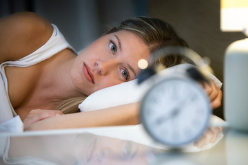 Beautiful young exhausted woman suffering insomnia lying on bed in bedroom at home.