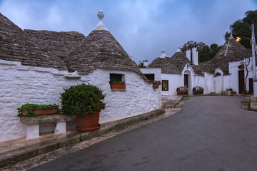 Fototapeta na wymiar Traditional white houses with conical roofs, flowers on street in Alberobello, Italy