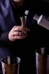 Bartender making refreshing coctail on a bar background. Dark moody style. Ice in tha glass