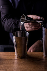 Bartender making refreshing coctail on a bar background. Dark moody style. Ice in tha glass
