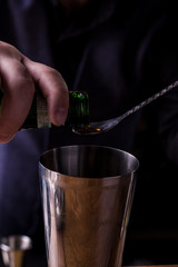Bartender making refreshing coctail on a bar background. Dark moody style. Ice in tha glass