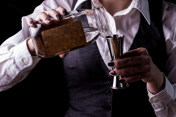 Bartender making refreshing coctail on a bar background. Dark moody style. Ice in tha glass